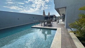 Un espace piscine aménagé sur le toit, avec des chaises longues et des parasols, entouré d’un bâtiment moderne.