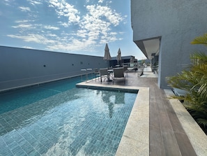 Área de piscina no terraço com espreguiçadeiras e guarda-sóis, em volta de um edifício moderno.