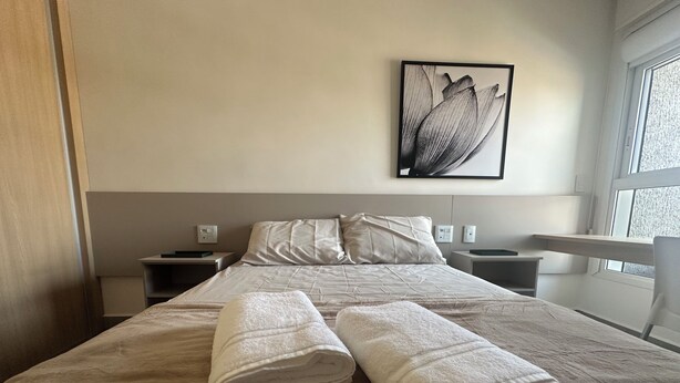 Une chambre d’hôtel avec un lit, deux tables de chevet, une œuvre d’art accrochée au mur et une fenêtre.