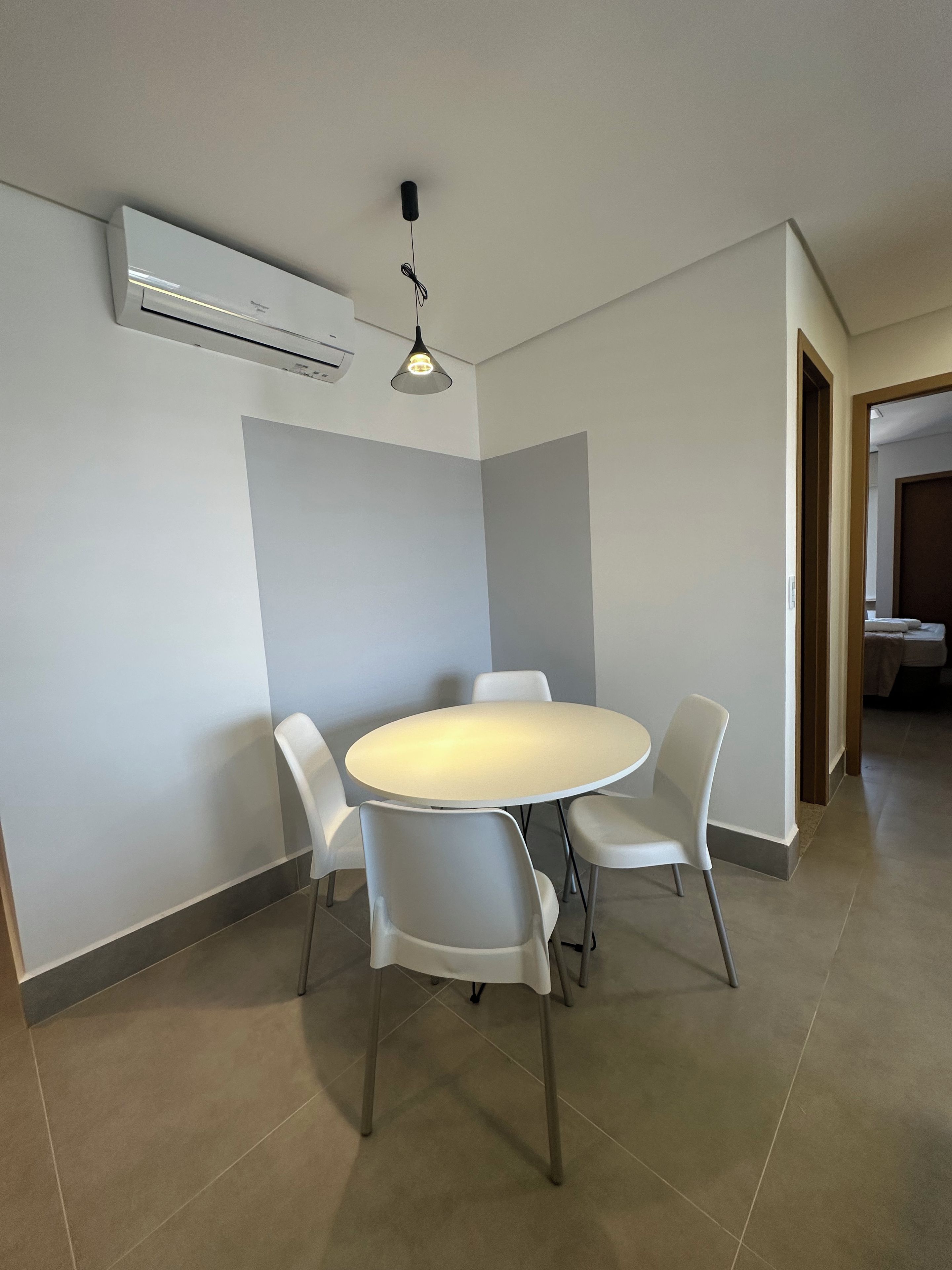 Une pièce avec une table ronde et quatre chaises, un appareil de climatisation et un luminaire suspendu.