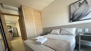 Une chambre d’hôtel comprenant un lit, une table de chevet, une lampe de chevet, une œuvre d’art accrochée au mur et donnant sur la chambre adjacente.