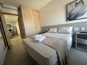 Quarto de hotel com cama, mesa de cabeceira, obra de arte na parede e vista para o quarto vizinho.