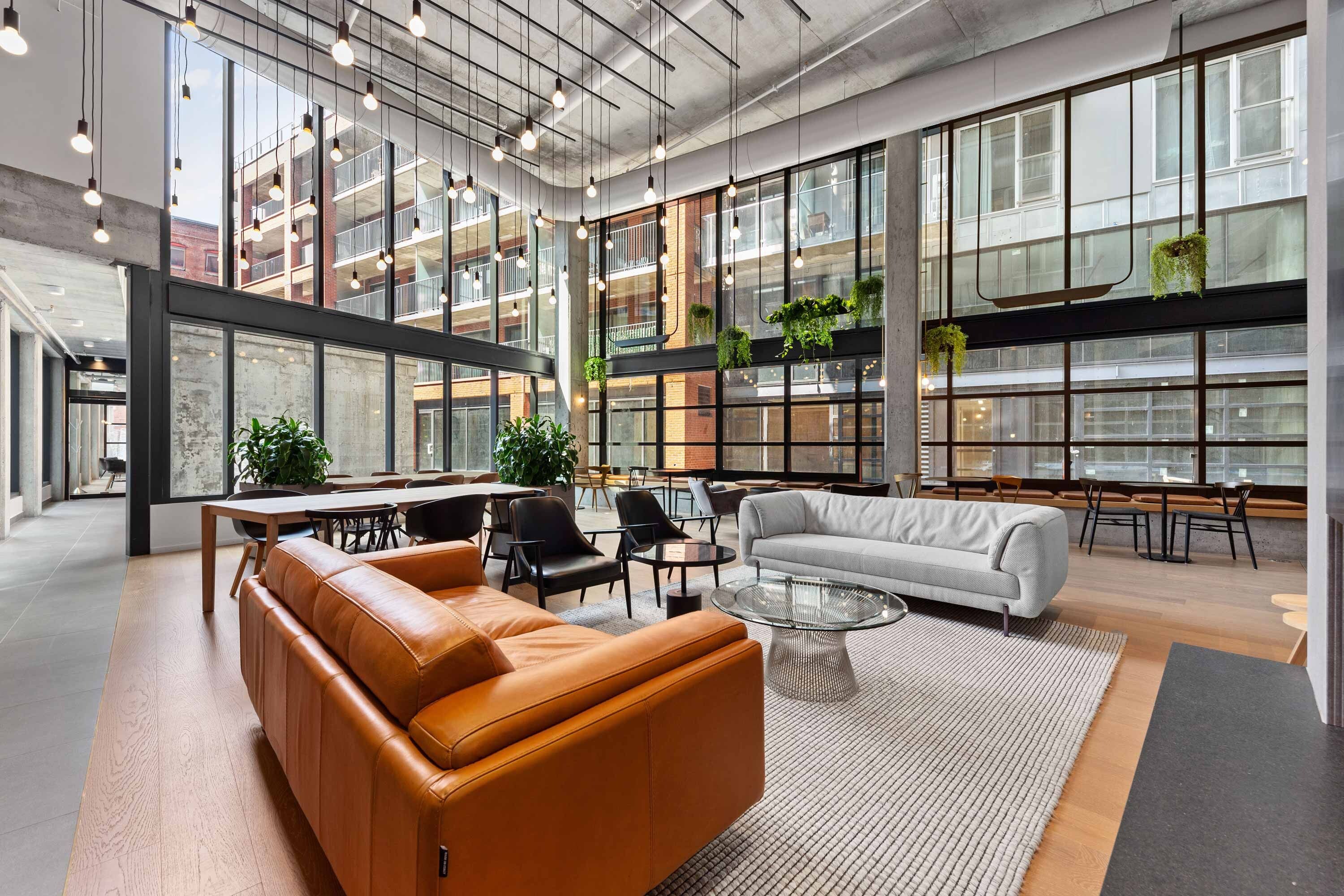 Un espacio interior amplio con techos altos, ventanas grandes y una variedad de opciones de asientos, incluyendo sofás y sillones.