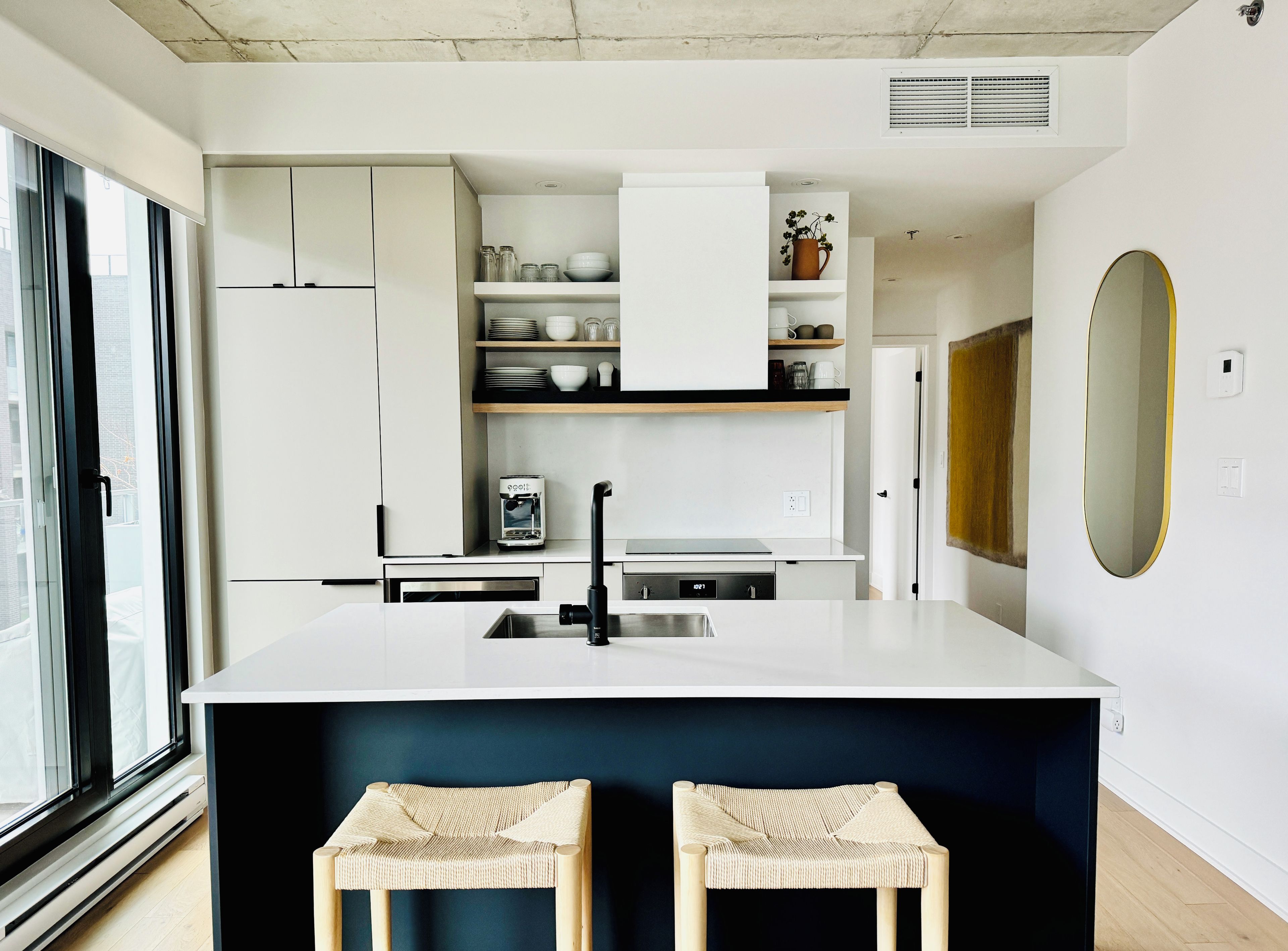 Una cocina moderna con muebles blancos, un dispensador de agua integrado y una isla grande con taburetes.