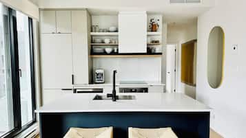 Una cocina moderna con muebles blancos, un dispensador de agua integrado y una isla grande con taburetes.