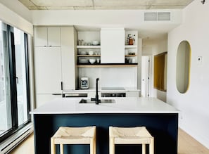 Una cocina moderna con muebles blancos, un dispensador de agua integrado y una isla grande con taburetes.