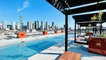 Una piscina en la azotea con vistas a un horizonte urbano, sillas de descanso y una zona de estar techada.