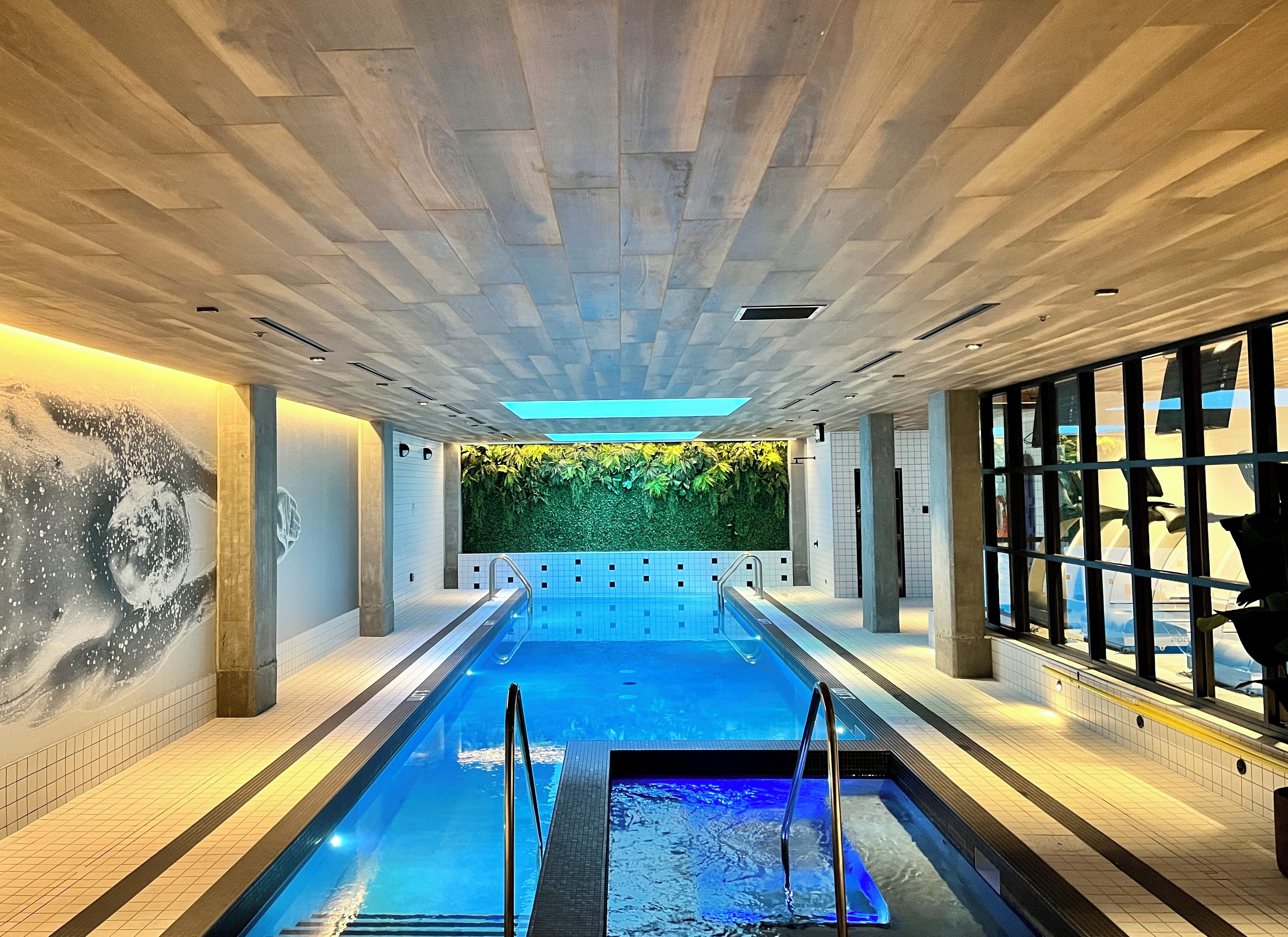 Una piscina con un borde empedrado, un mural en la pared y una pared verde con plantas.
