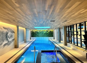 Una piscina con un borde empedrado, un mural en la pared y una pared verde con plantas.