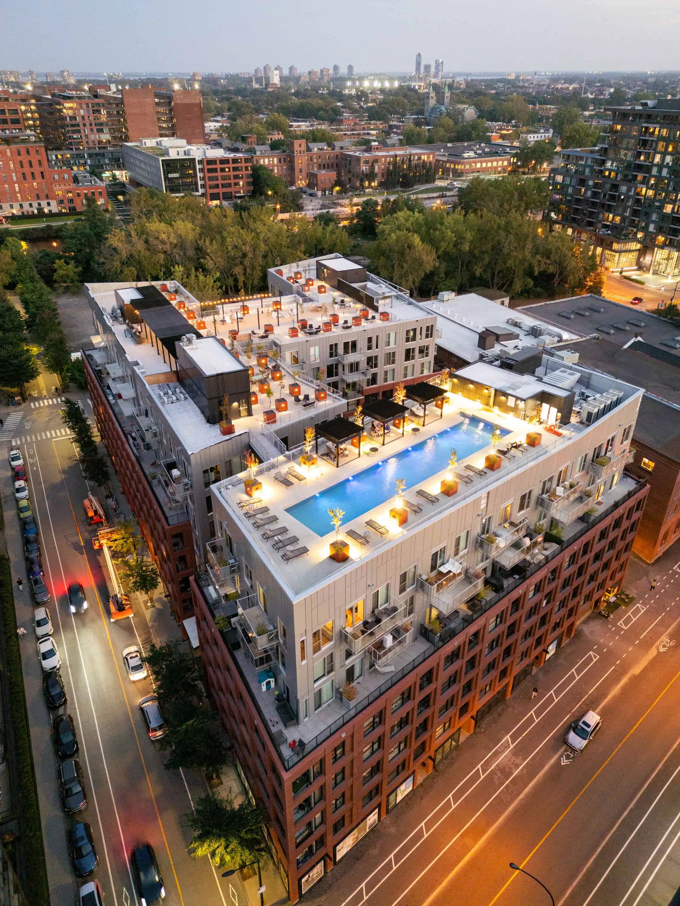 Un hotel de varios pisos con piscina en la azotea, rodeado por un paisaje urbano.
