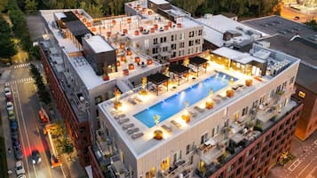 Un hotel de varios pisos con piscina en la azotea, rodeado por un paisaje urbano.
