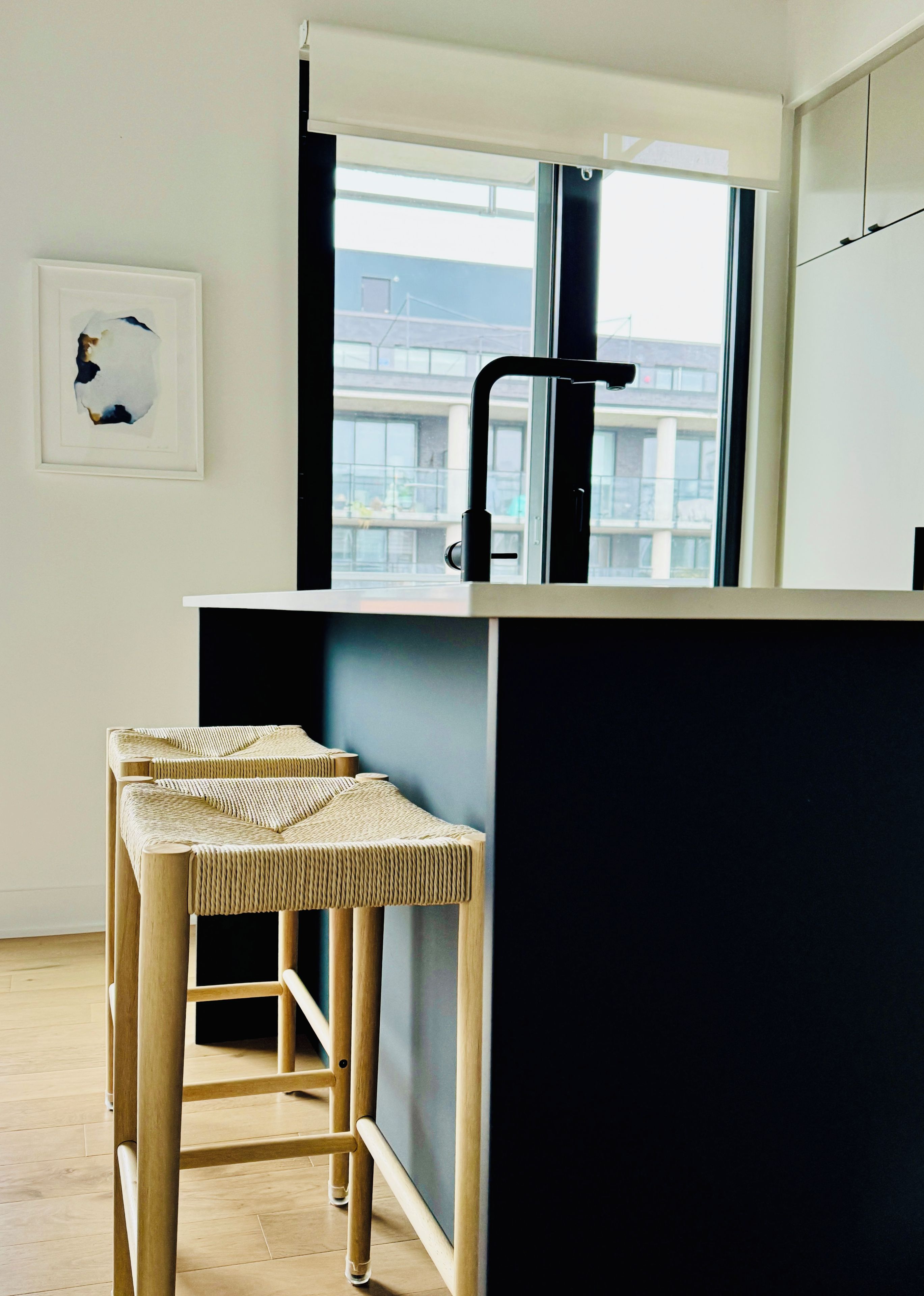 Una cocina moderna con encimera negra, ventana y dos taburetes de fibras naturales.
