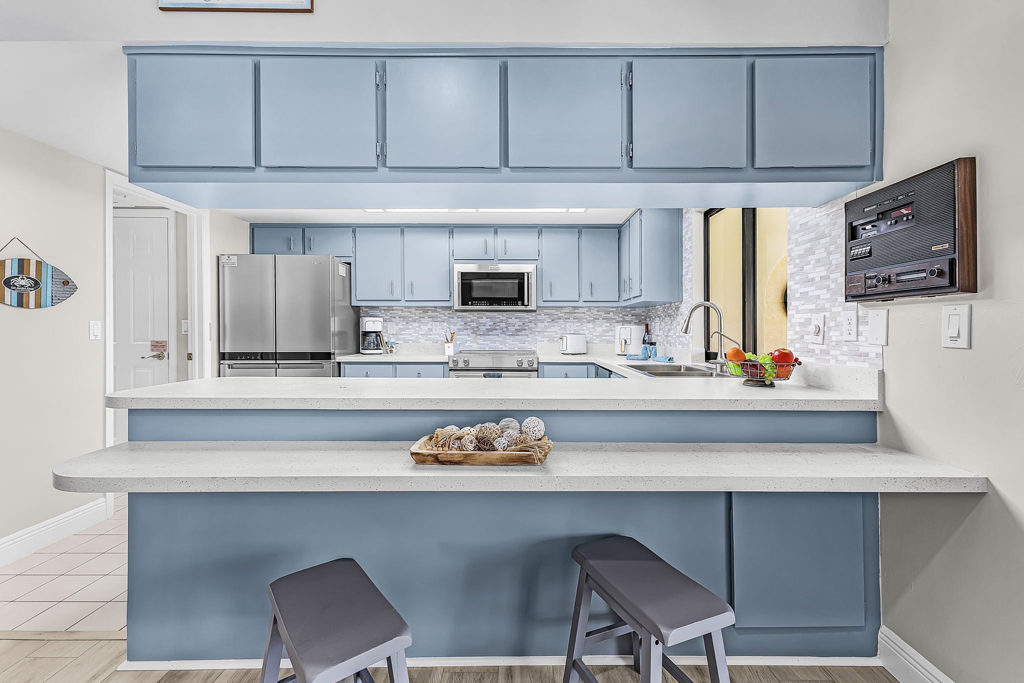 A modern kitchen with blue cabinets, stainless steel appliances, a large island with stools, and a decorative wall piece.