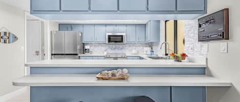 A modern kitchen with blue cabinets, stainless steel appliances, a large island with stools, and a decorative wall piece.