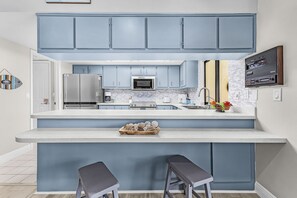 A modern kitchen with blue cabinets, stainless steel appliances, a large island with stools, and a decorative wall piece. - Poolside Escape for Family Fun in Sunny Cape Coral Getaways - Country Club Villa - Roelens (Cape Coral)