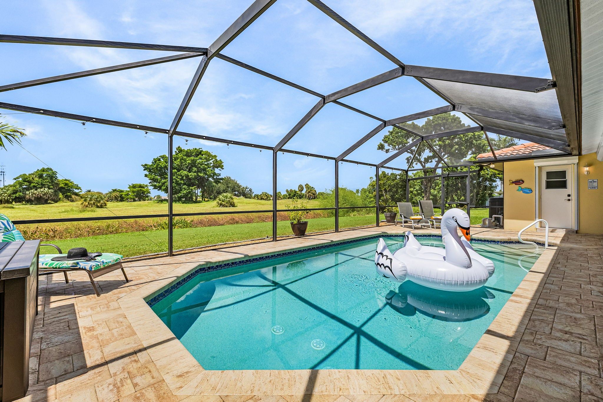 A covered outdoor swimming pool with a swan inflatable, surrounded by a patio area with chairs and a table.
