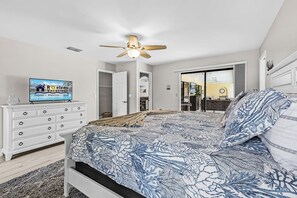 A bedroom with a bed, a TV, a dresser, and a ceiling fan. - Poolside Escape for Family Fun in Sunny Cape Coral Getaways - Country Club Villa - Roelens (Cape Coral)