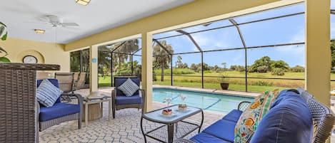 A sunlit patio with a pool, wicker furniture, and a view of the landscape.