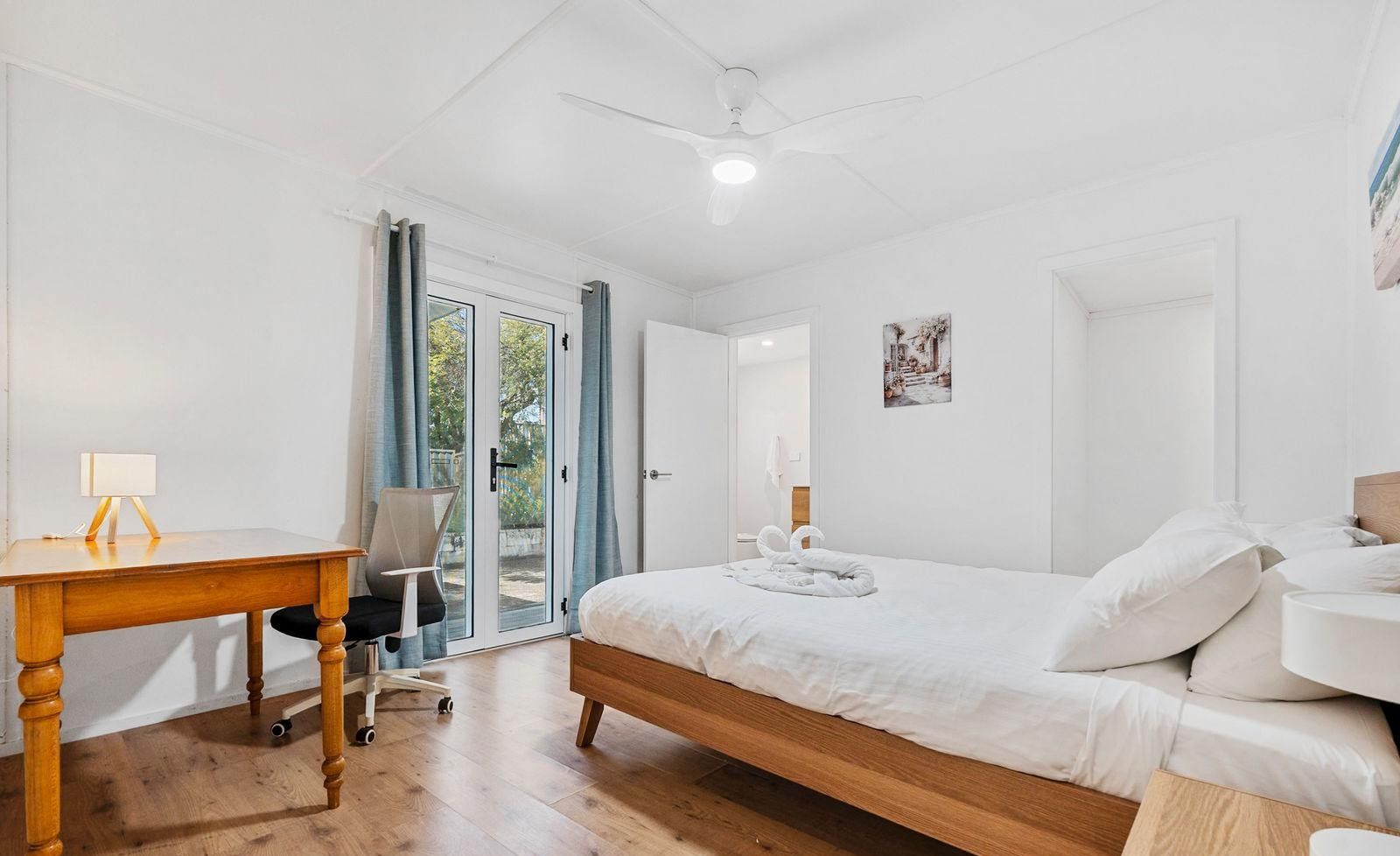 A bedroom with a wooden bed, a desk with a lamp, a chair, and a ceiling fan.