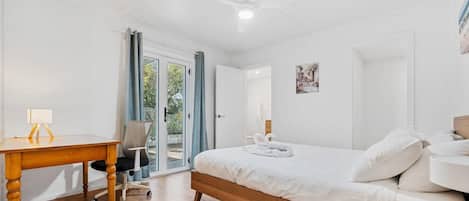 A bedroom with a wooden bed, a desk with a lamp, a chair, and a ceiling fan.