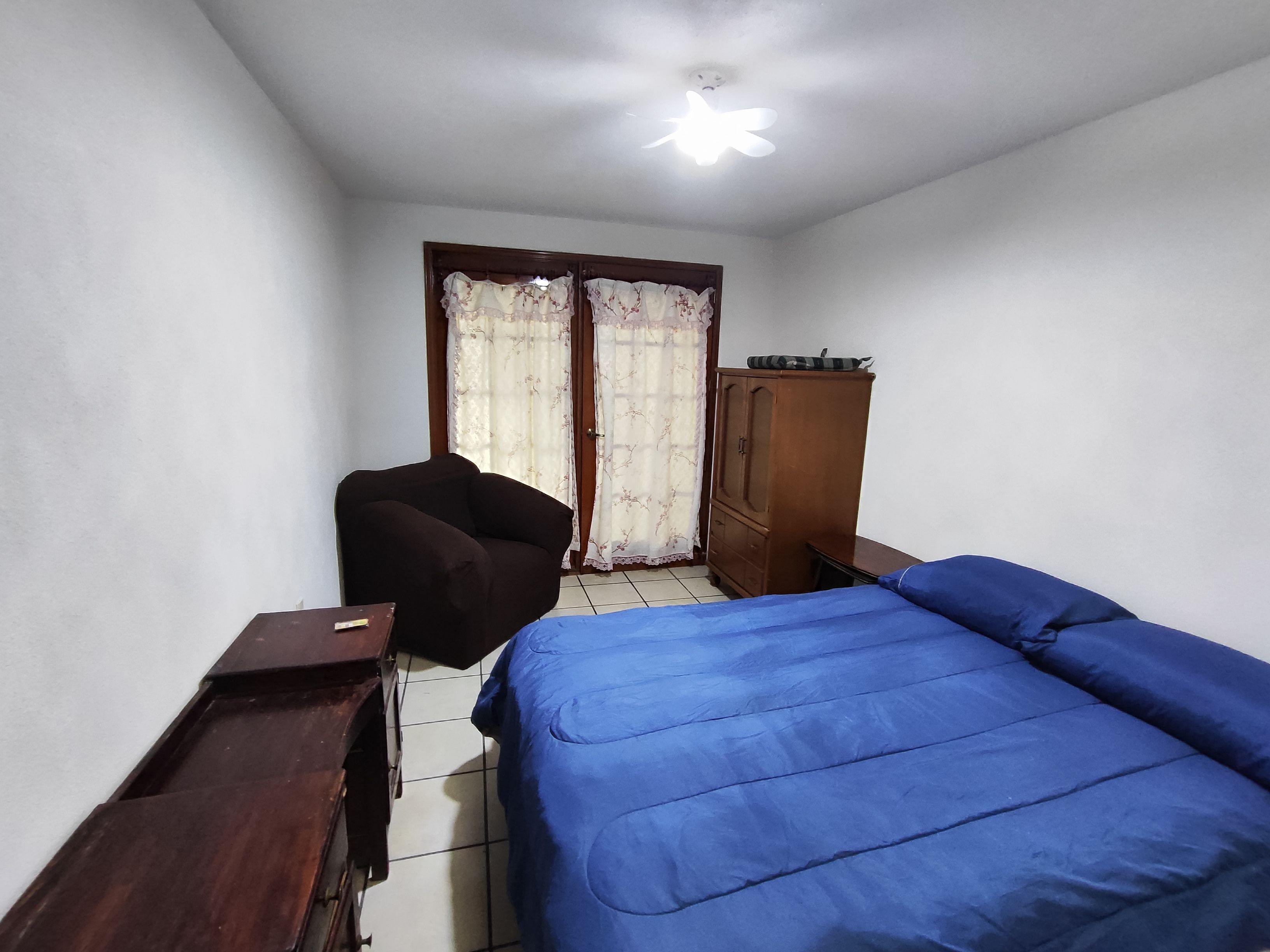 A bedroom with a bed, a chair, a wardrobe, and a ceiling fan.