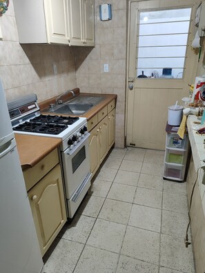 A compact kitchen with a gas stove, oven, and sink. There is a window with horizontal blinds, and a small storage unit with containers. - Extraordinary house in Los Pinos, Morelia (wheelchair accessible). (Morelia)