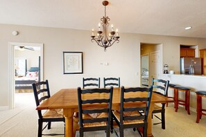 A dining room with a wooden table and chairs, a chandelier, and a kitchen in the background. - Aerie Retreat | Mtn Views, Near Sugar Ski Resort (Sugar Mountain)