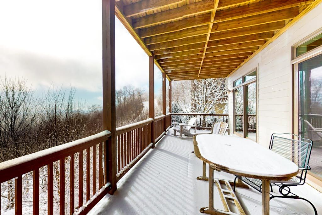 A covered outdoor deck with a table and chairs, overlooking a snowy landscape.
