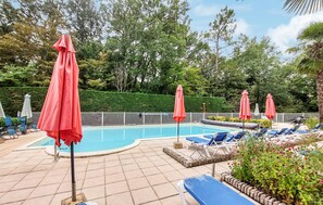 Ein Poolbereich mit Liegestühlen und Sonnenschirmen, umgeben von einer Hecke und Pflanzen.