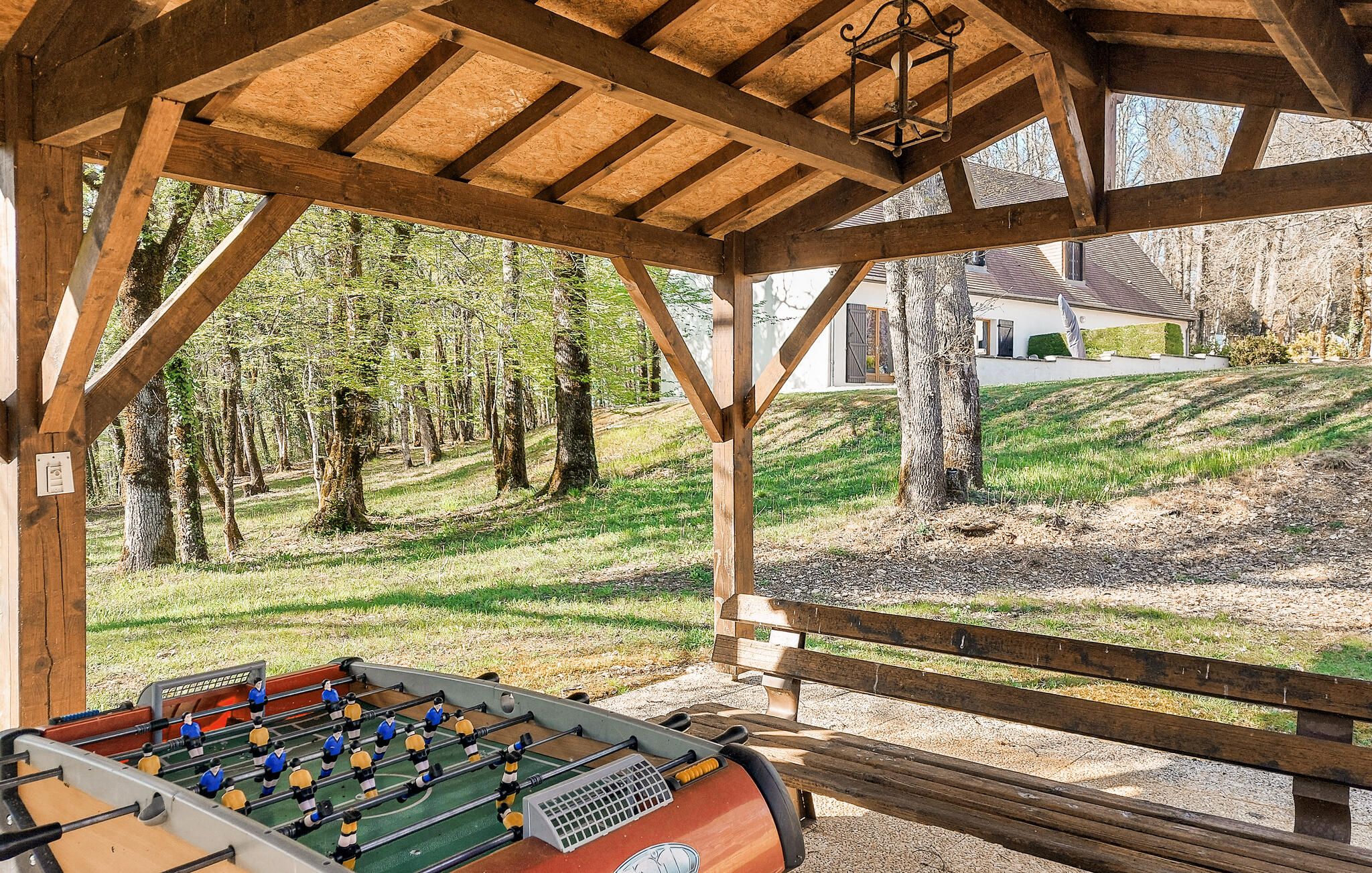 Un kiosque en bois avec une table de baby-foot, entouré d’arbres et d’une pelouse.