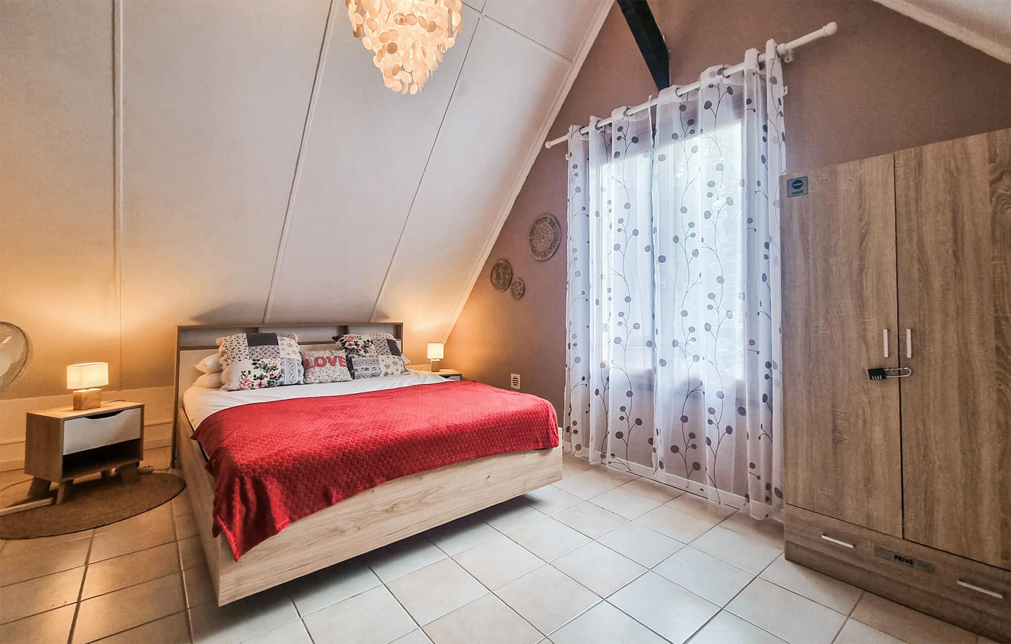 A bedroom with a bed, a wardrobe, a nightstand, a lamp, and a ceiling light fixture.
