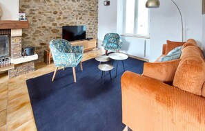 En stue med stenvæg, fjernsyn, to møblerede stole, et lille bord og en orange sofa.