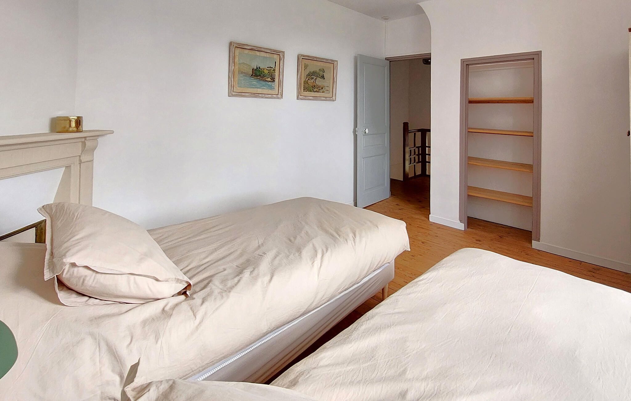 Ein Schlafzimmer mit zwei Betten, Holzboden, einer weißen Tür und einem Gang zu einem anderen Zimmer.