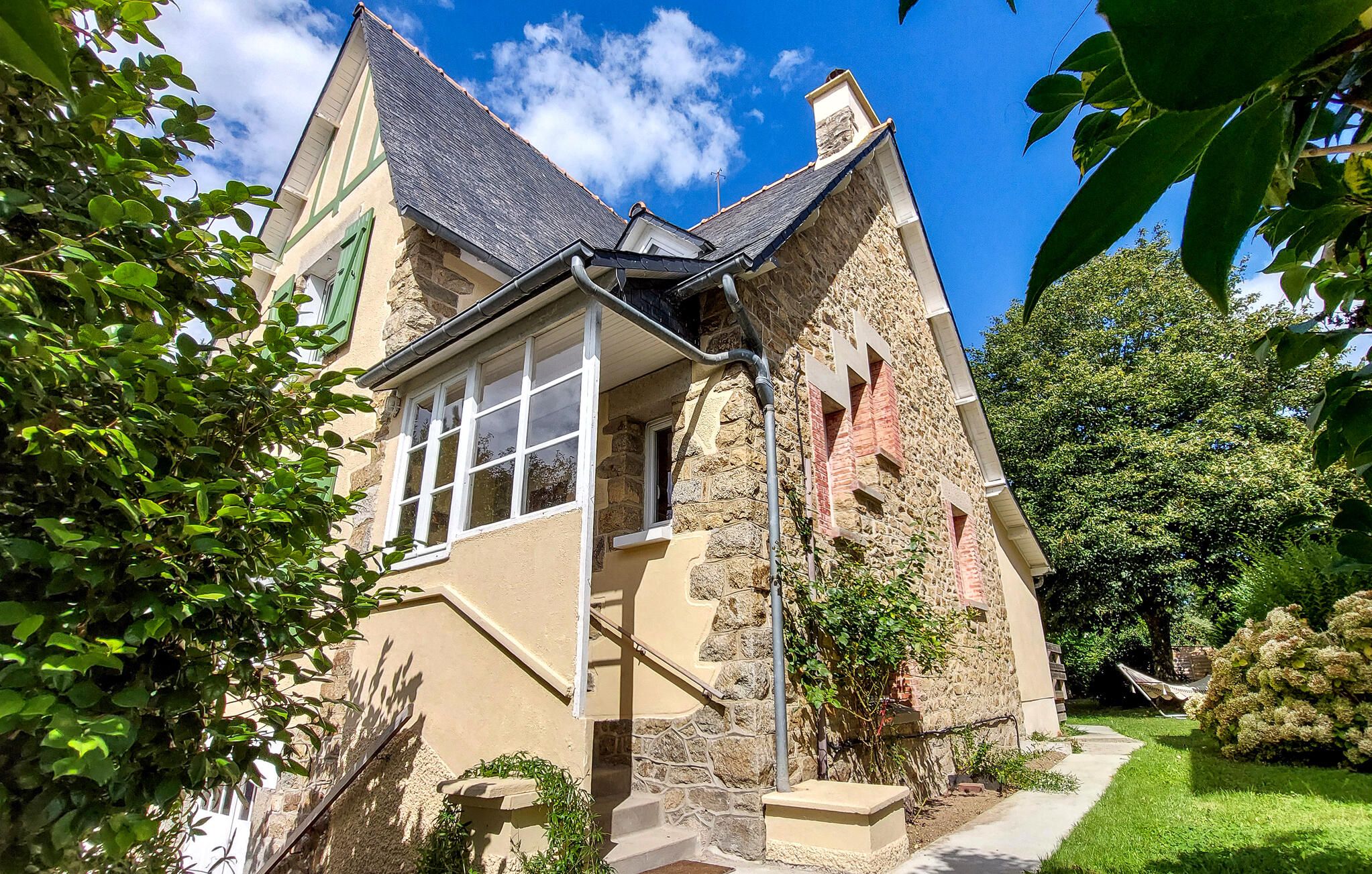 Une maison en pierre avec un toit à pignon, une fenêtre visible et un jardin avec un sentier.