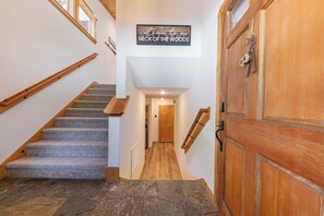 A wooden staircase with carpeted steps leading to a door labeled 'NECK OF THE WOODS.' - Monthly Lease - Bellflower at Tahoe Donner by Tahoe Getaways - Pet-Friendly 4BR w EV Charger & HOA (Truckee)