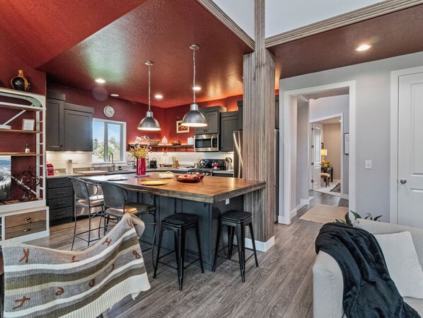 A modern kitchen with a central island, bar stools, pendant lighting, and a view of the outdoors. - Midway 447 | Golf Views | Gym | Pool & Hot Tub | Near Deer Valley (Midway)