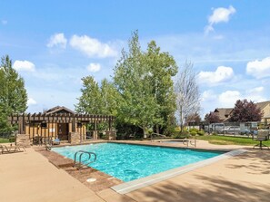 A swimming pool with a wooden deck and lounge chairs, surrounded by trees and a building with a pergola. - Midway 447 | Golf Views | Gym | Pool & Hot Tub | Near Deer Valley (Midway)