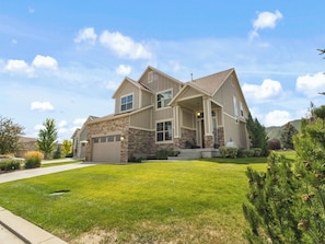A two-story house with a garage, a front porch, and a well-maintained lawn. - Midway 447 | Golf Views | Gym | Pool & Hot Tub | Near Deer Valley (Midway)