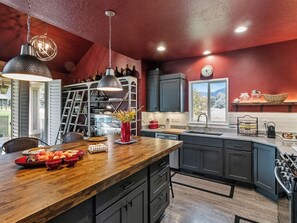 A modern kitchen with a wooden island, dark cabinets, and a red accent wall. - Midway 447 | Golf Views | Gym | Pool & Hot Tub | Near Deer Valley (Midway)