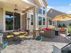 An outdoor patio area with a dining table, chairs, a fire pit, and a stone pillar. - Midway 447 | Golf Views | Gym | Pool & Hot Tub | Near Deer Valley (Midway)