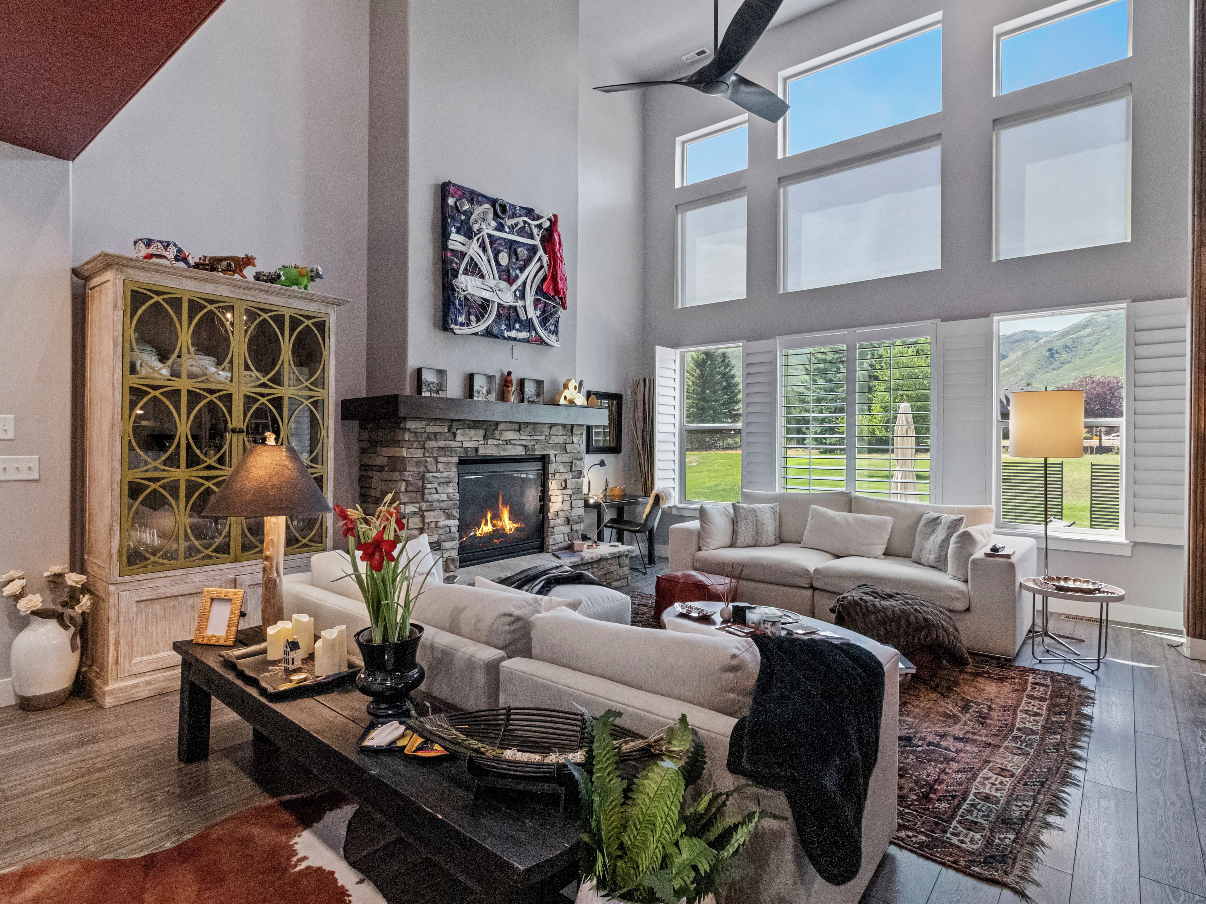 A spacious living room with a fireplace, a large window with a view of the outdoors, and a ceiling fan.