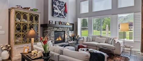 A spacious living room with a fireplace, a large window with a view of the outdoors, and a ceiling fan.