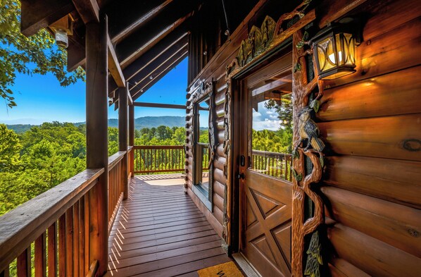 A wooden cabin with a balcony overlooking a forested landscape.