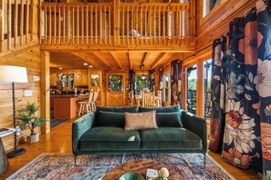 A wooden cabin interior with a green sofa, a dining area, and a kitchen.