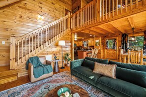 A wooden interior with a staircase, a sofa, a dining area, and a kitchen.