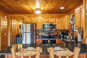 A wooden cabin interior with a kitchen featuring a refrigerator, microwave, stove, and wooden cabinets. - Firefly Forest • Stunning Mtn Views • Hot Tub • Sauna • Firepit • 5 Min to Pkwy! (Pigeon Forge)