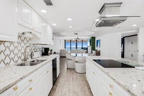 A modern kitchen with white cabinetry, granite countertops, and a central island. - ⭐CBC 1-20E | Penthouse beachfront condo with Gulf views, 2BR/2BA, pool, gym, and balcony. (Clearwater Beach)
