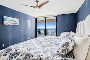 Ein Schlafzimmer mit Bett, Deckenventilator, Gemälde und Blick auf den Ozean.