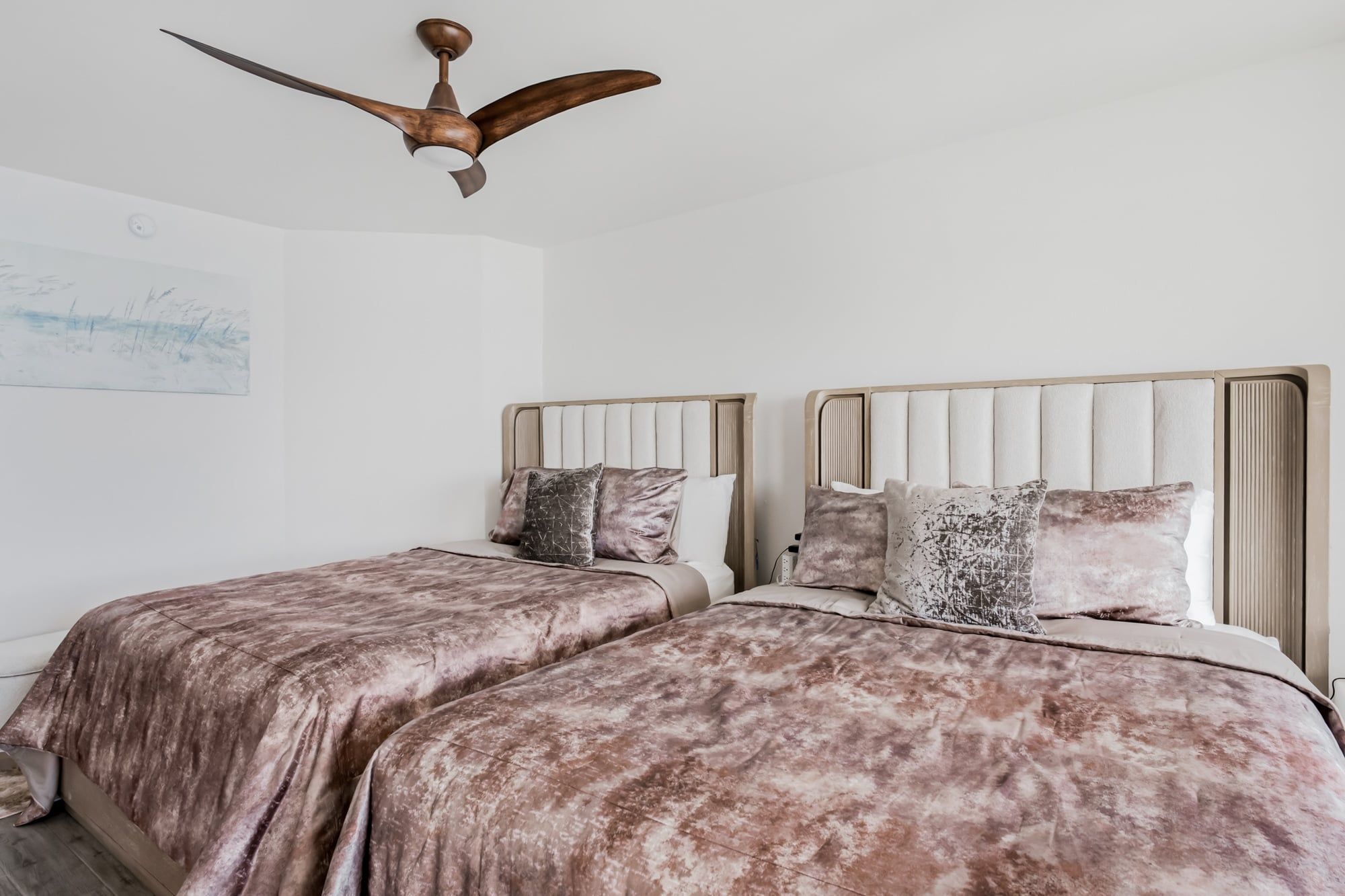 A bedroom with two beds, a ceiling fan, and a wall with a painting.