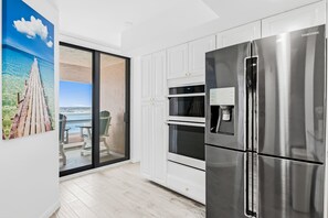 Una cocina moderna con refrigerador de acero inoxidable, armarios blancos y una puerta corrediza de vidrio que da a un área exterior con vista a un muelle.